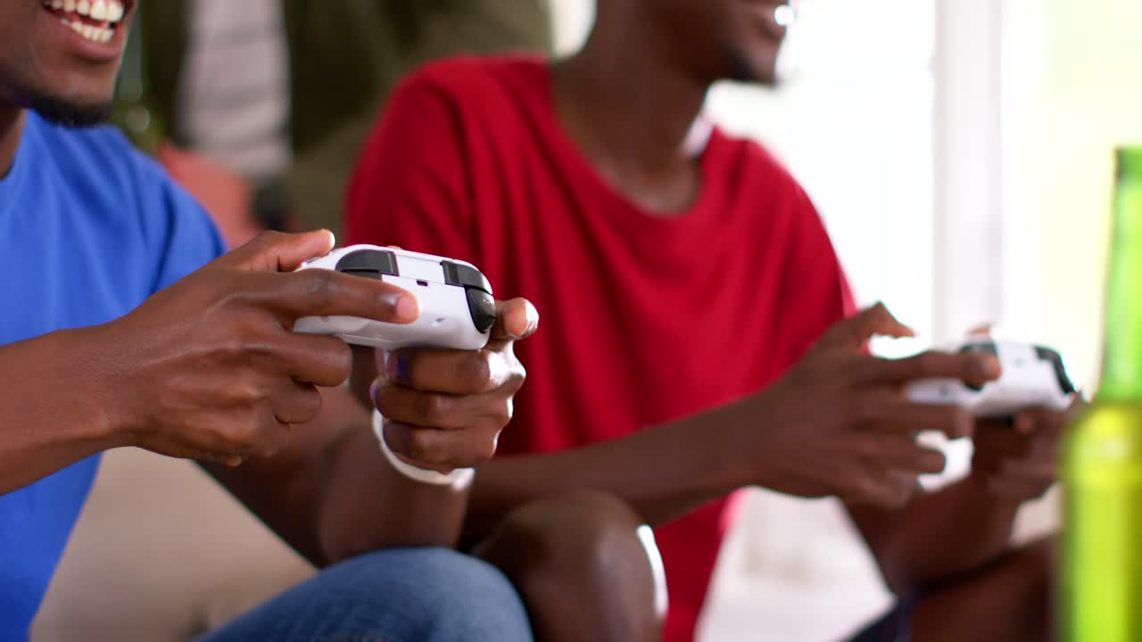 African American male friends starting game, competing, pressing white gamepads, laughing on couch