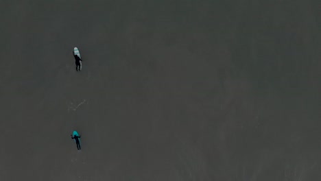 two surfers on their surfboards paddling with hands in the ocean at nantasket beach in hull, massachusetts - aerial top-down