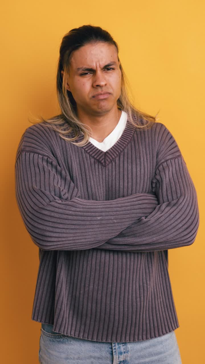 Annoyed Young Man with Long Hair Crossing Arms on Yellow Background