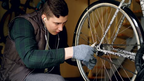 un tipo serio y experimentado está arreglando las articulaciones del mecanismo de ajuste de la rueda de la bicicleta usando instrumentos profesionales. la rueda giratoria con radios metálicos brillantes está en primer plano.