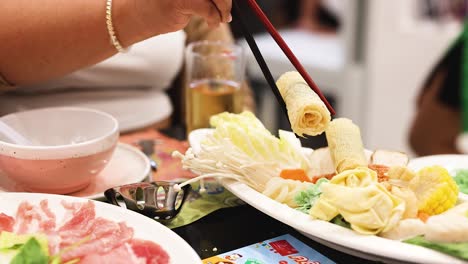 chopsticks picking food from a hotpot platter