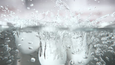 los huevos con cáscaras blancas caen en una olla de agua hirviendo y se hunden en el líquido caliente, macro y cámara lenta