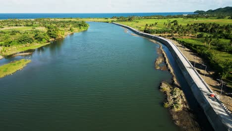 aerial drone shot of scenic provincial river along boulevard walkway amid lush tropical island valley at pajo river, catanduanes, philippines