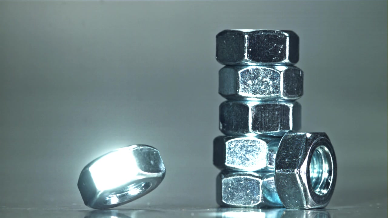 Shiny Metal Nut Rolling on a Surface Next to a Stack of Nuts