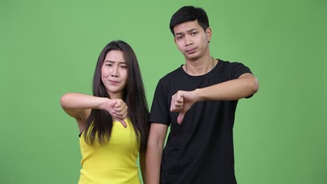 young sad asian couple giving thumbs down together