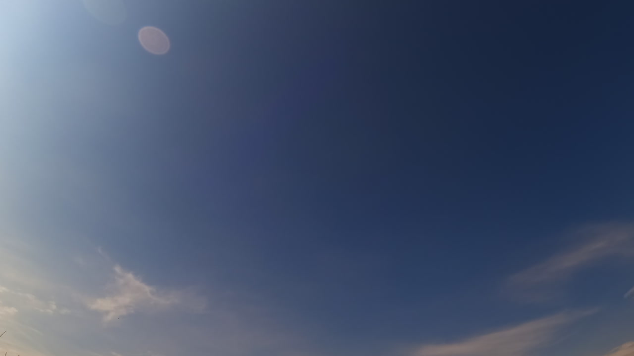 Tiny light small clouds appear in the blue sky. Low angle view at the sky in summer. Timelapse