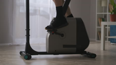 가정에서 훈련하기위한 현대적인 정지 자전거: 페달에 있는 남성의 다리의 근접한 시각, 신체적 및 스포츠 활동, 남자가 체력을 유지하고 있습니다.