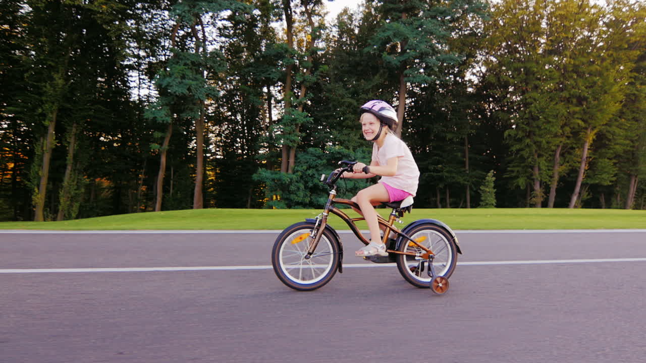 나무를 배경으로 잘 관리된 공원에서 자전거를 타는 헬멧을 쓴 5년 된 소녀
