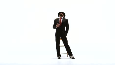 man in suit and hat posing with a chair on white background