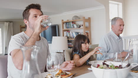 multi generation family sitting around table at home eating meal together