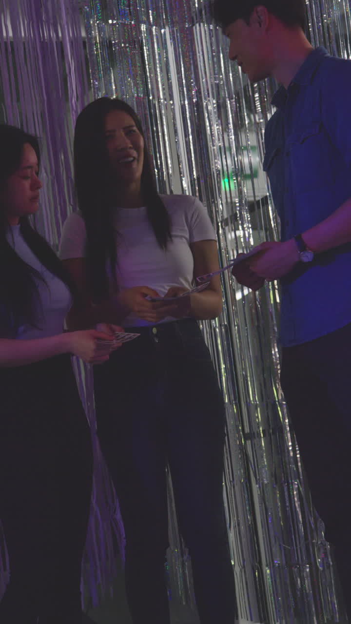 una toma de video vertical de un grupo de amigos divirtiéndose mirando las impresiones de la cabina de fotos 3