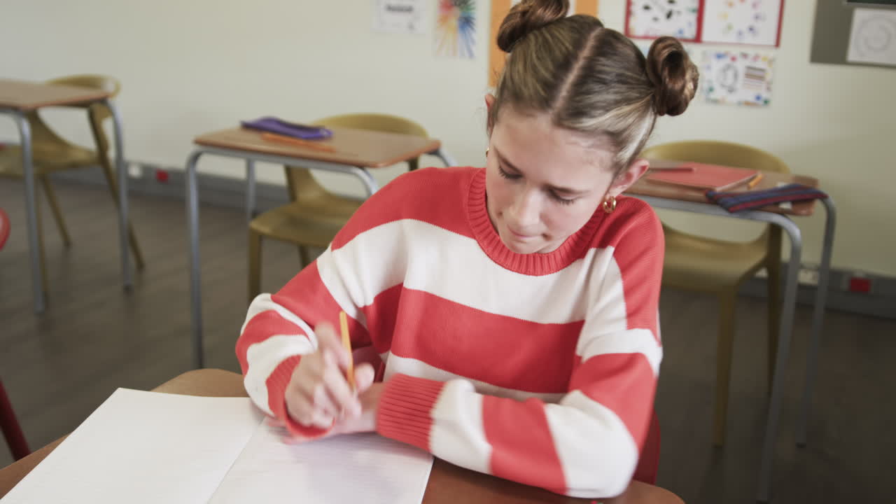 In school, girl writing in notebook at desk, concentrating on assignment
