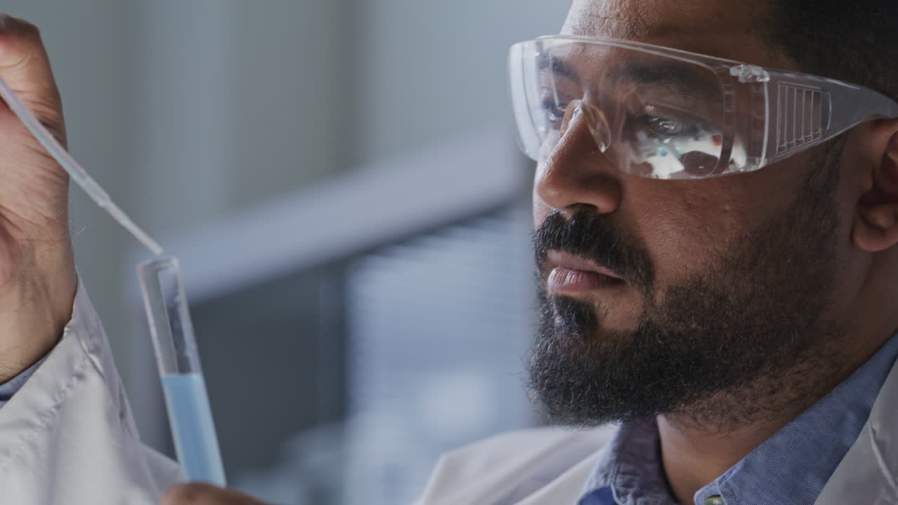 Scientist in Safety Goggles Pouring Blue Liquid with Pipette into Test Tube