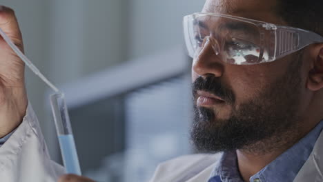 scientist in safety goggles pouring blue liquid with pipette into test tube
