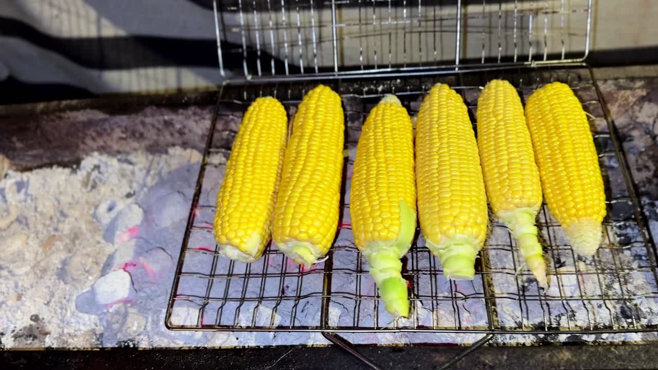 4K close up of golden corn roasting on a charcoal grill with glowing embers and ash showing detailed texture warm tones and a rustic outdoor cooking atmosphere