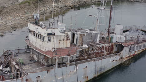 rusty grey half submerged shipwreck anchored near the shore on a cloudy overcast day