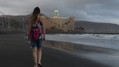 Fantastische-Sonnenuntergangsaufnahme-Einer-Frau,-Die-Am-Strand-Von-Las-Canteras-Spazieren-Geht-Und-Im-Hintergrund-Das-Auditorium-Von-Alfredo-Kraus-Sieht