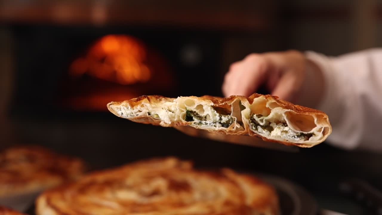 Mano che regge un burek appena sfornato con ripieno di formaggio e spinaci