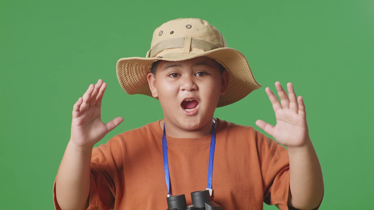 모자를 입은 아시아 관광 소년은 안경을 통해 바라본 후 와우라고 말합니다. 소년 연구자는 녹색 화면 배경에서 무언가를 조사합니다. 여행 관광 모험 개념, 근접