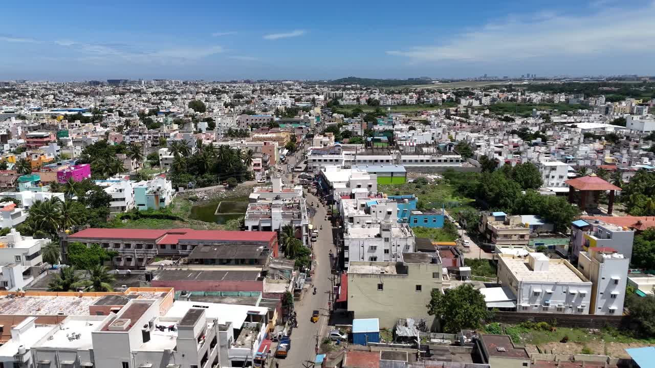 High-angle aerial shot over a tightly packed South Asian city, showing a mix of low-rise residential and commercial buildings. The scene conveys a busy, developing urban centre. Near to airport runway