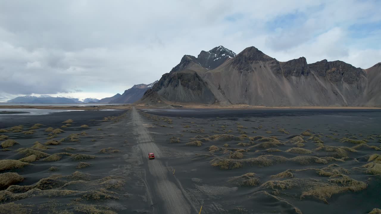 video de drones de la playa de arena negra stokksnes vestrahorn en islandia con un auto rojo conduciendo por un camino de tierra