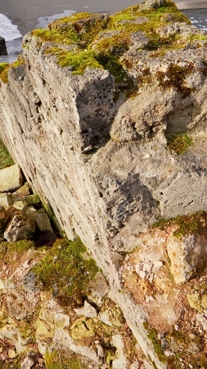 Close-up of a crumbling historic wall with fallen stones and moss beside worn steps, showing structural decay, weather damage, and neglected heritage masonry in a park setting.