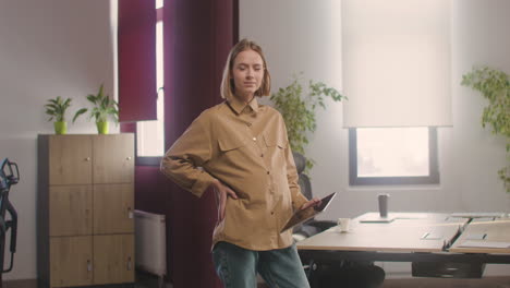 Pregnant-Woman-Posing-At-Camera-While-Holding-A-Tablet-In-The-Office