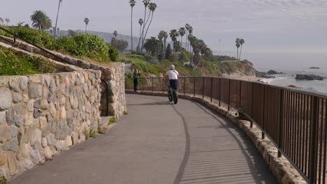 Hombre-Caucásico-Montando-Una-Bicicleta-Eléctrica-Por-Un-Camino,-Con-Vista-Al-Océano,-En-Laguna-Beach,-California