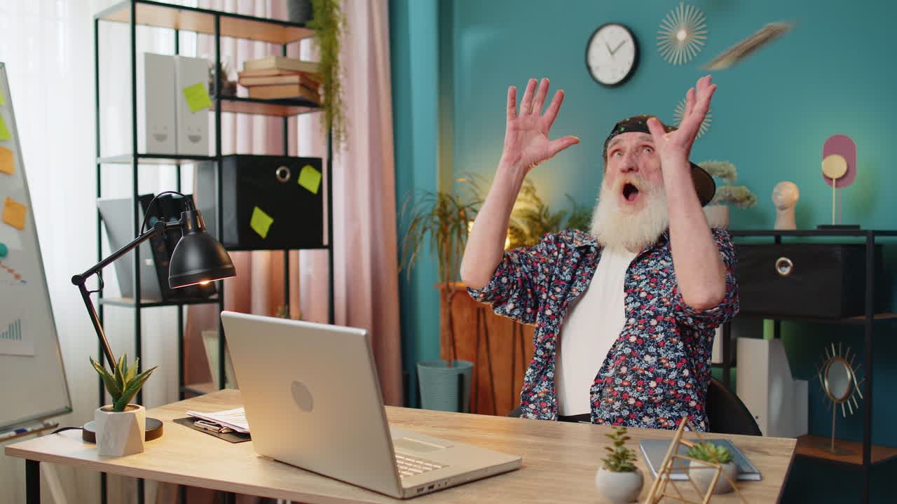 деньги в долларах падают на пожилого человека с ноутбуком, празднующего успех, победу, достижение цели.