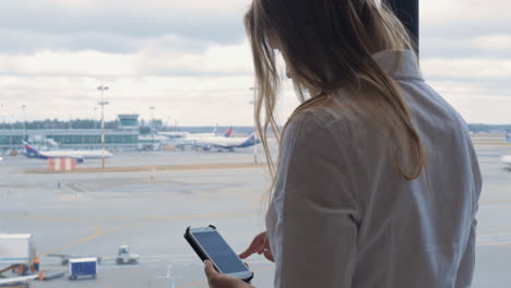 mujer enviando mensajes de texto en el móvil y mirando el área del aeropuerto