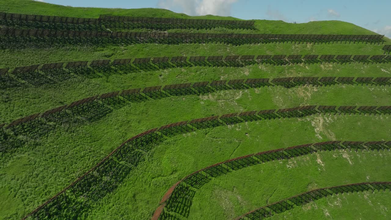 Terraced green slopes with snow barriers in the Austrian Alps near Berwang, aerial view