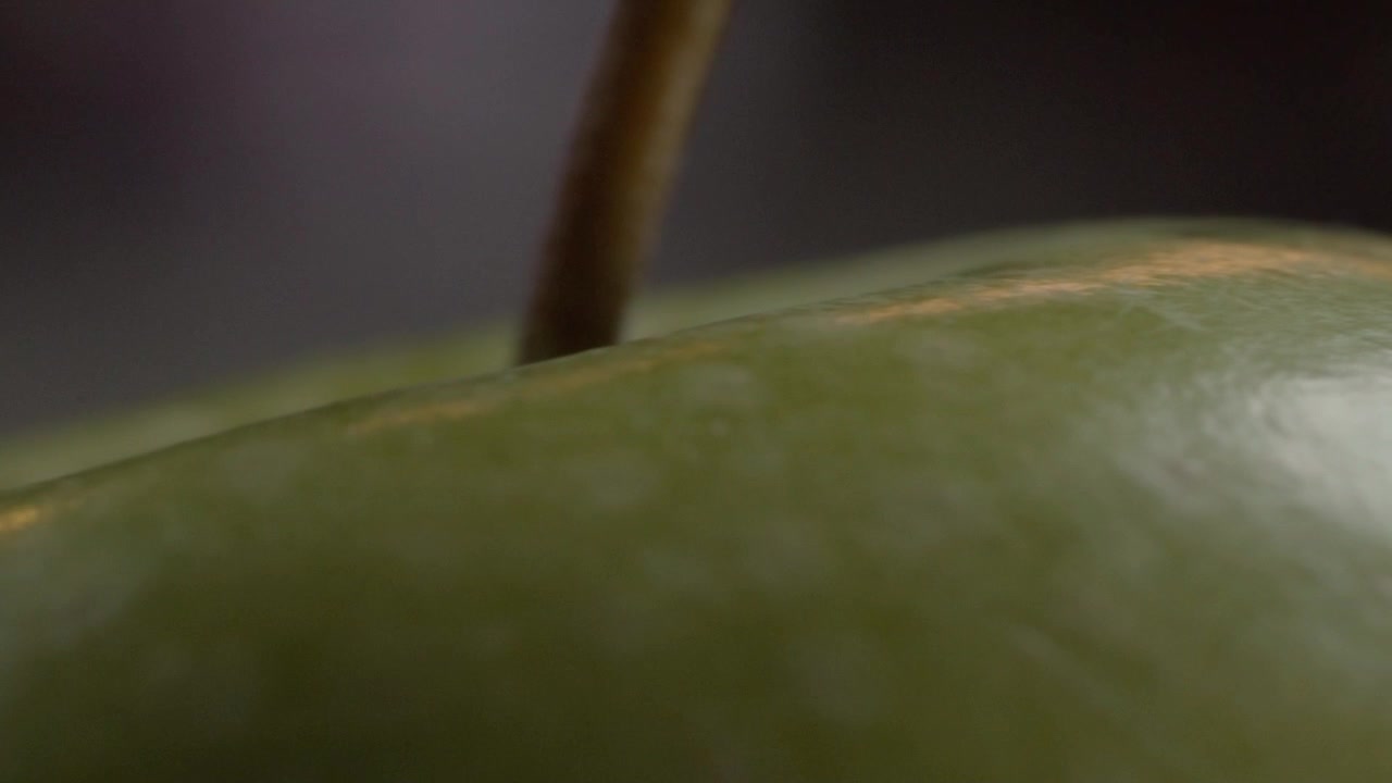 Extreme close up of a green apple showing detailed skin texture and a visible stem, with shallow focus emphasizing the curved fruit surface in Mexico.