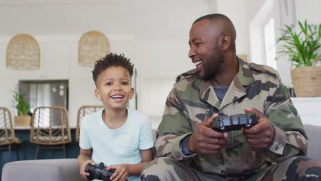 Happy-african-american-father-and-his-son-sitting-on-sofa-and-playing-video-games