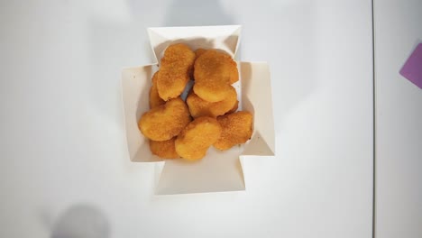 hands taking nuggets from paper box on table. top view. unrecognizable people simultaneously spreading arms to get pieces of