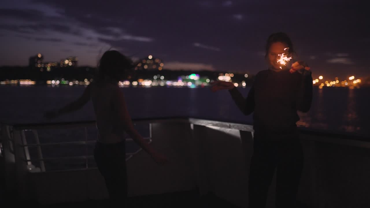 밤에 배 갑판에서 춤을 추는 두 명의 아름다운 젊은 여성의 실루. 배에 있는 여자 친구