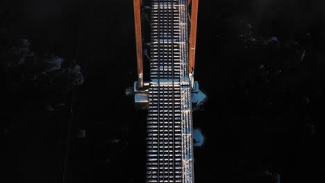 aerial top down flying over the snow covered rail road trestle crossing a cold dark river at sunrise