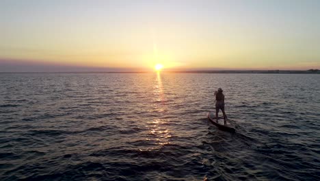 paddleboarder paddling away into the sunset.