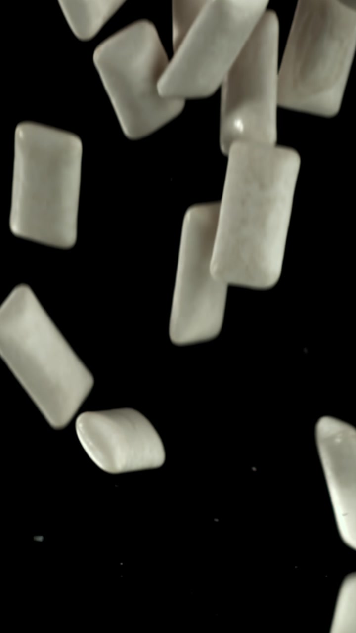 Pezzi di gomma da masticare bianchi che cadono al rallentatore su una superficie nera riflettente