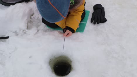 small kid ice fishing on a frozen river in winter in norway