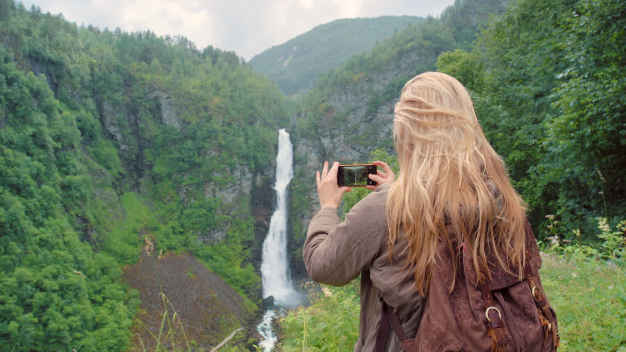 mujer tomando una foto de una cascada en noruega