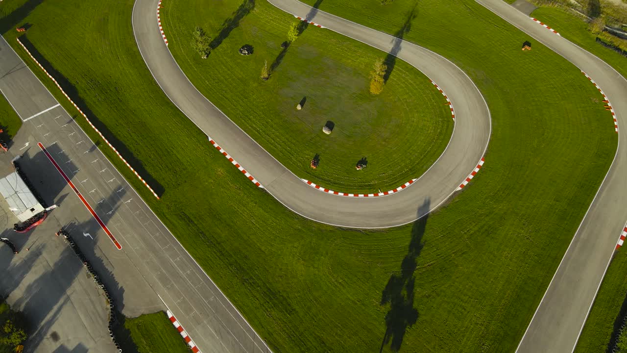 Aerial drone video of a modern Go Karting racing speedway or racing track in grassy green countryside during autumn sunny day. Asphalt roads are clean and curved with mowed lawn around the corners