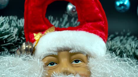 Detailed-close-up-smooth-tilt-up-shot,-Santa-Claus-toy-in-a-red-hat-with-bells,-Christmas-decoration,-traditional-holiday-presents,-new-year-decor,-shiny-colorful-gifts,-4K-video