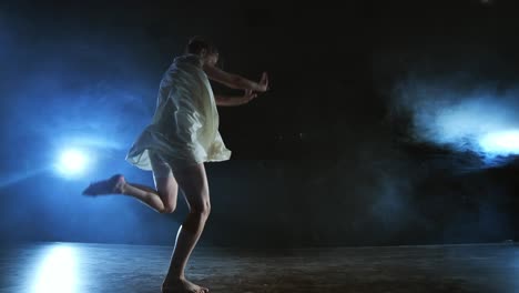 una joven bailarina descalza salta al escenario y se mueve en cámara lenta en un vestido blanco suelto