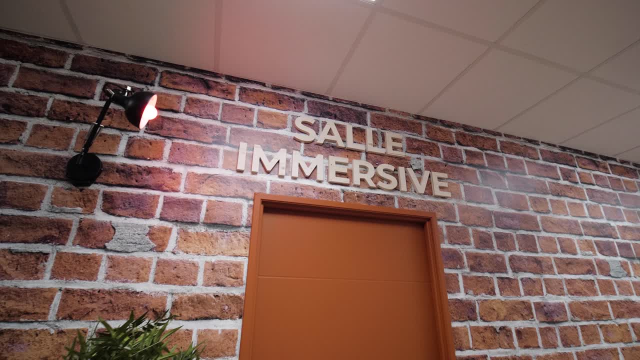 entrada de la habitación inmersiva con pared de ladrillo, puerta naranja y iluminación moderna