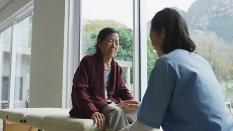 smiling asian female physiotherapist treating knee of senior female patient and talking at surgery