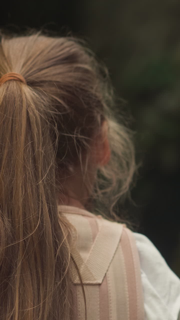 의료 코르을 입은 소녀는 폭포를 가까이에서 바라보고 있습니다. 등통을 가진 아이는 재활을 겪고 있습니다. 흐릿한 배경에서 자연에서 시간을 보내고 있습니다.