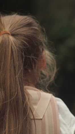 girl in medical corset stands looking at waterfall closeup backside view. child with back pain undergoes rehabilitation spending time in nature on blurred background