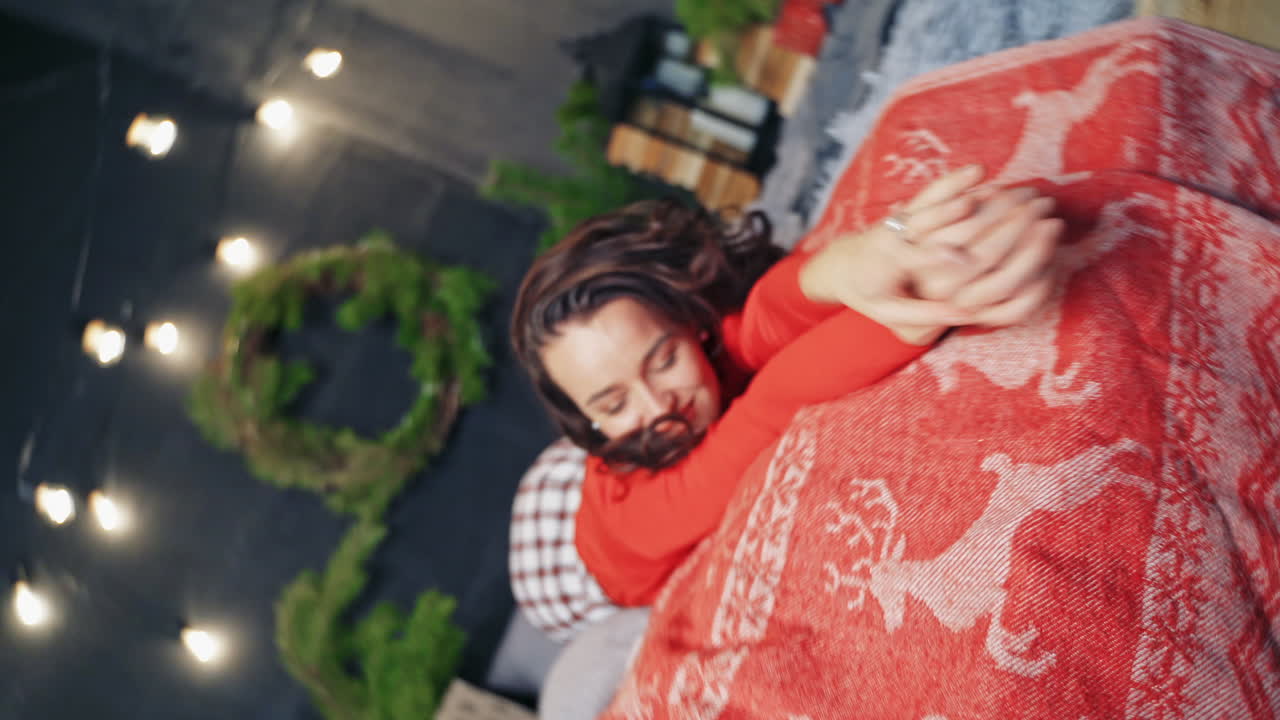 Happy woman on Christmas decorations background. Young woman in red sweater is lying on the bed with pleasure in winter holidays. Happy winter holidays concept.