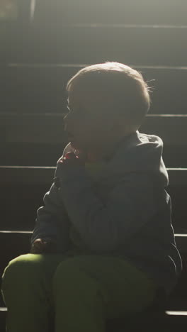 little child sitting on stairs silhouette in evening. boy enjoys calm night resting on steps at country house. kid spends time on pouch at backlight