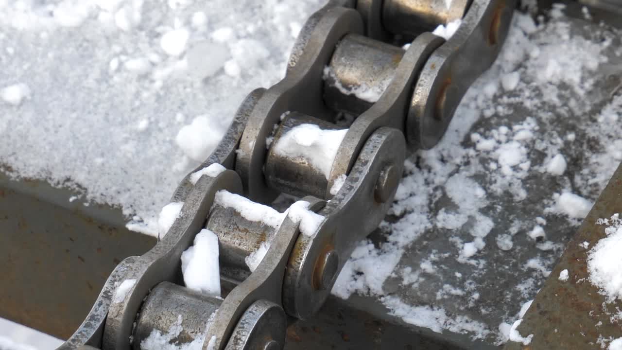 A steel roller chain conveyor system covered in snow is used to transport ice blocks to Harbin. The industrial mechanism operates in extreme winter conditions.
